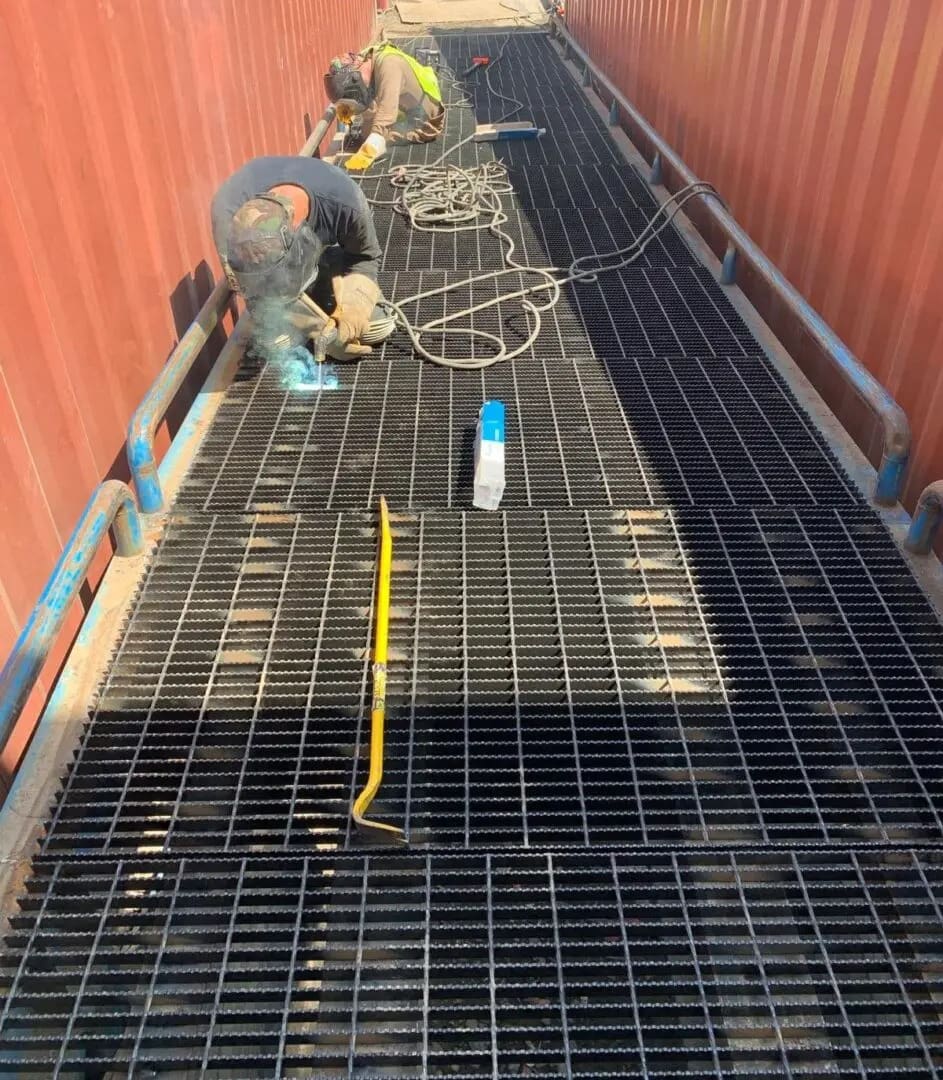 Workers welding metal grating in container